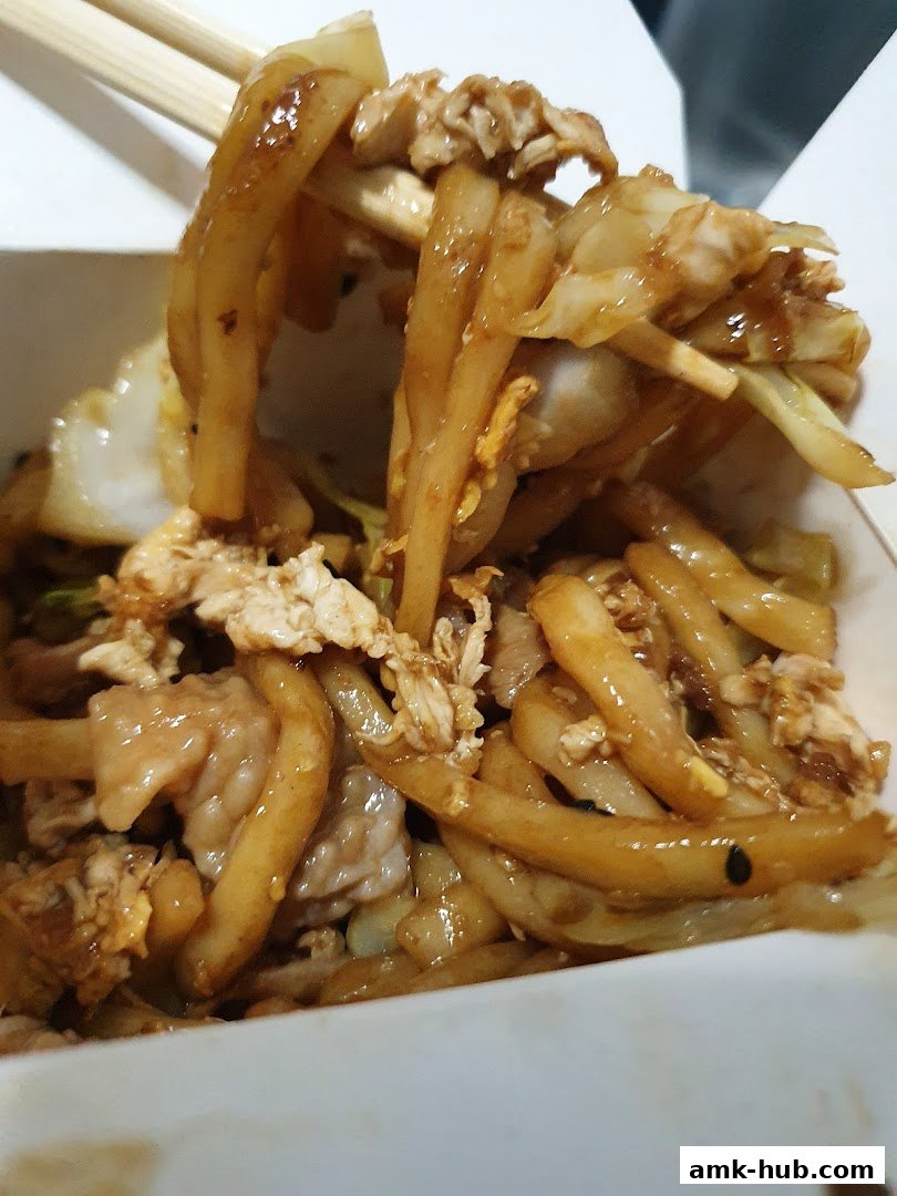 A close-up shot of delicious stir-fried noodles with chicken and vegetables being lifted by chopsticks.