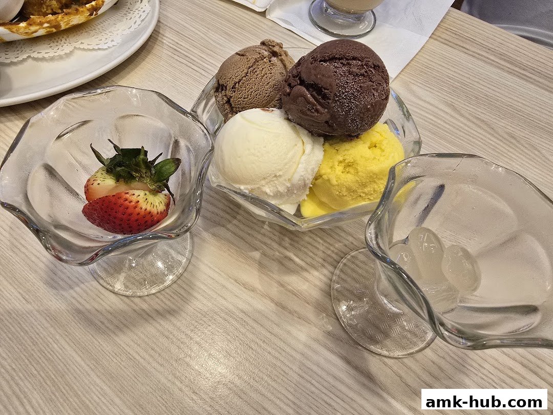 A close-up of several scoops of ice cream in glass bowls, with a strawberry and ice cubes.