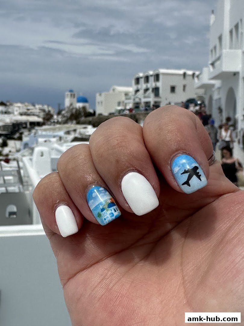 A hand with white and travel-themed nails, featuring an airplane and Greek architecture.