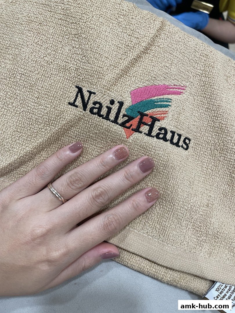 A close-up of a hand with freshly manicured nails resting on a beige towel with the Nailz Haus logo.