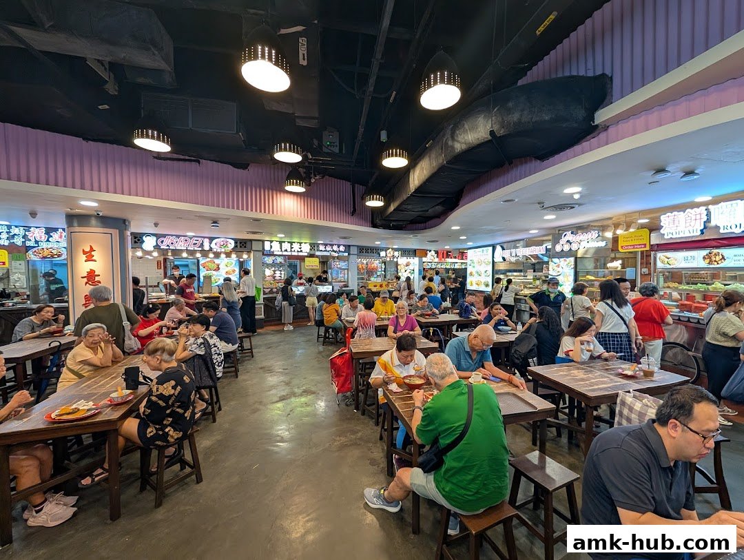 A bustling food court with many people dining at tables and ordering food from various stalls.