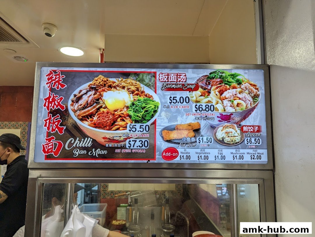 A menu board displays various noodle dishes and side items with prices.
