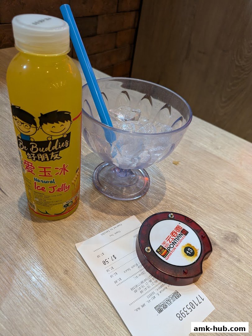 A bottle of yellow ice jelly drink, a glass of ice, and a receipt on a wooden table.