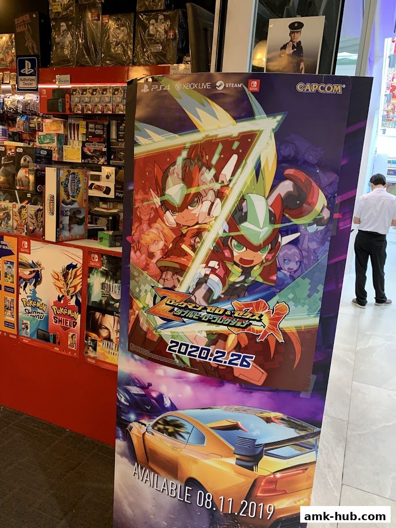 A display poster for a video game featuring anime characters and cars, with game consoles and merchandise in the background.