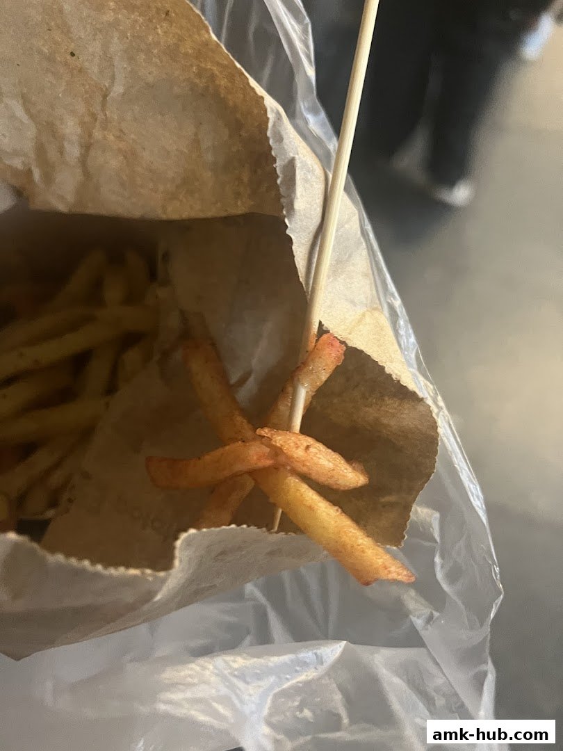 A close-up of seasoned french fries served in a paper bag with a skewer.