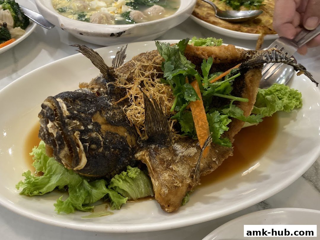 A whole fried fish dish served with lettuce, carrots, and a savory sauce.