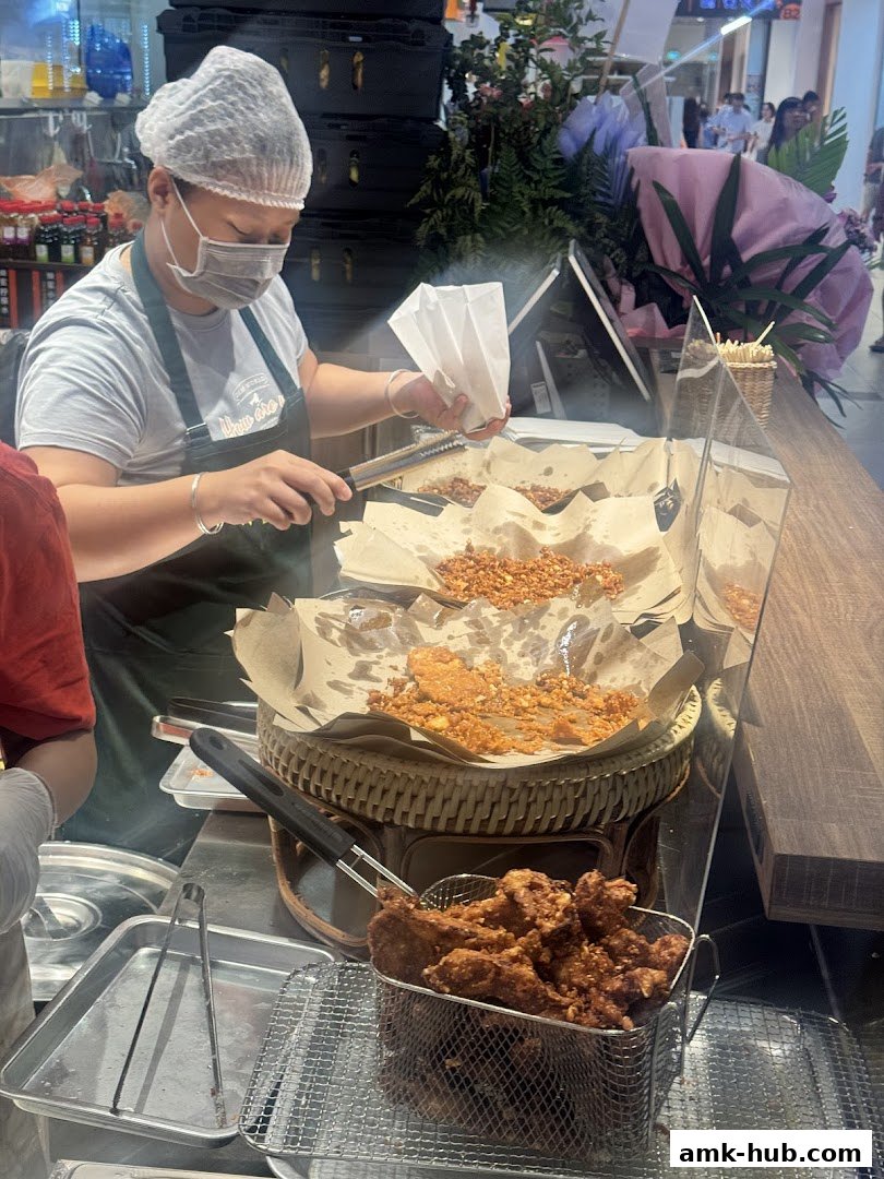 A vendor prepares fried snacks at a food stall, with a basket of fried items in the foreground.