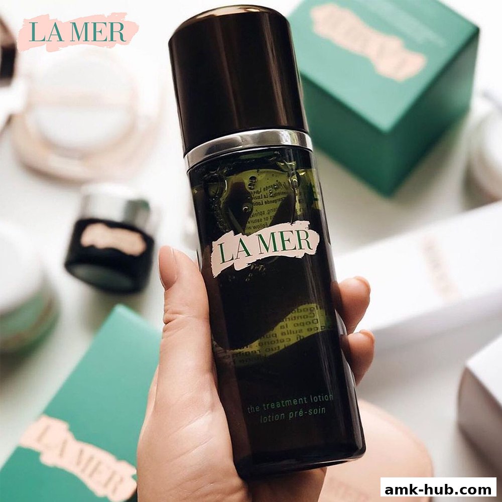 A hand holds a bottle of La Mer The Treatment Lotion surrounded by other La Mer products.