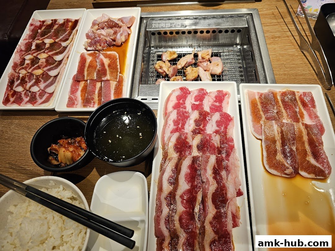 A table laden with various cuts of raw meat, kimchi, rice, and soup, ready for grilling.