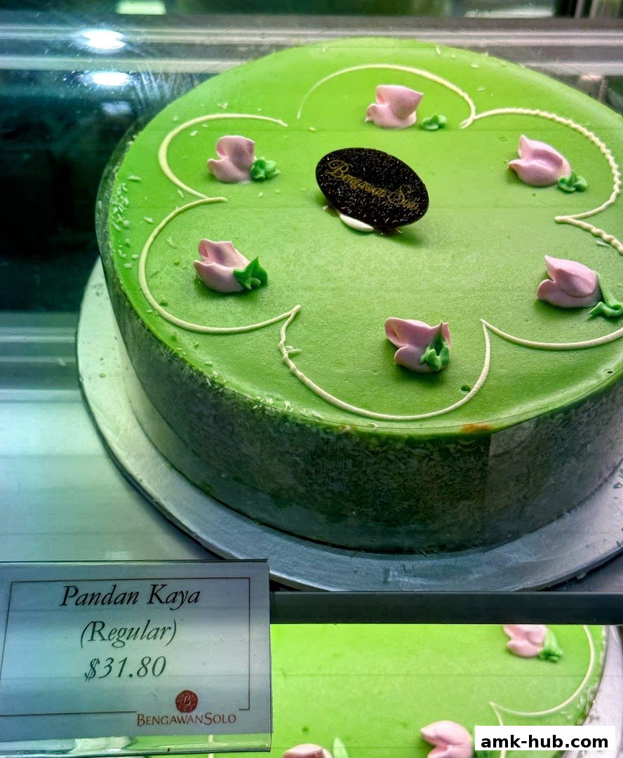 A green Pandan Kaya cake with pink floral decorations and a price tag.