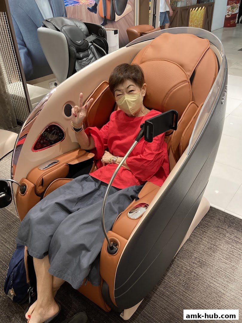 A woman sits in a massage chair, smiling and giving a peace sign.