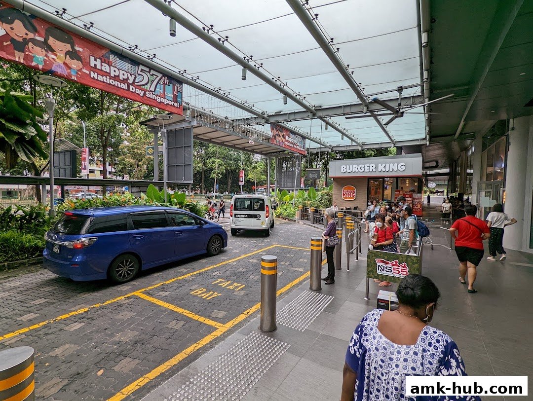 A Burger King restaurant entrance with a queue of people and a taxi bay outside.