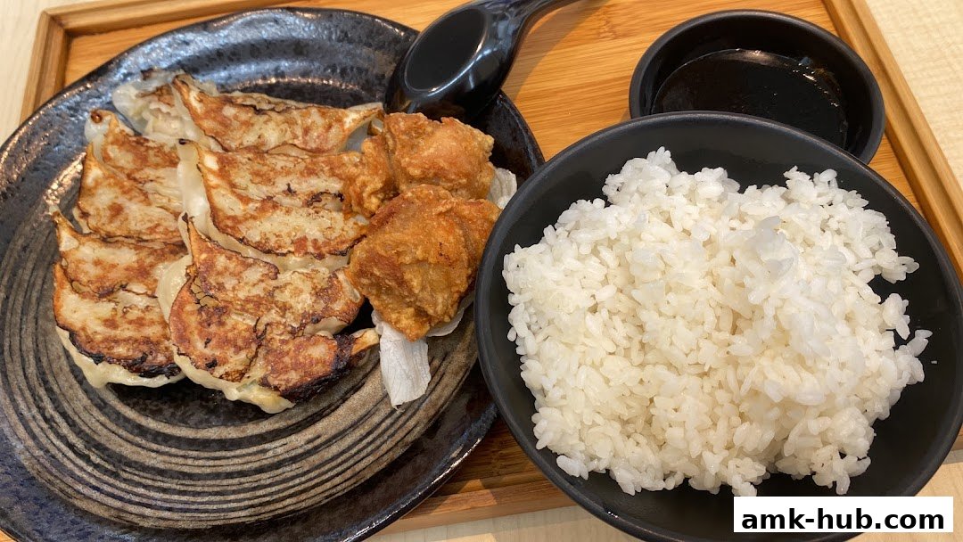 A plate of pan-fried gyoza and fried chicken served with a bowl of white rice.