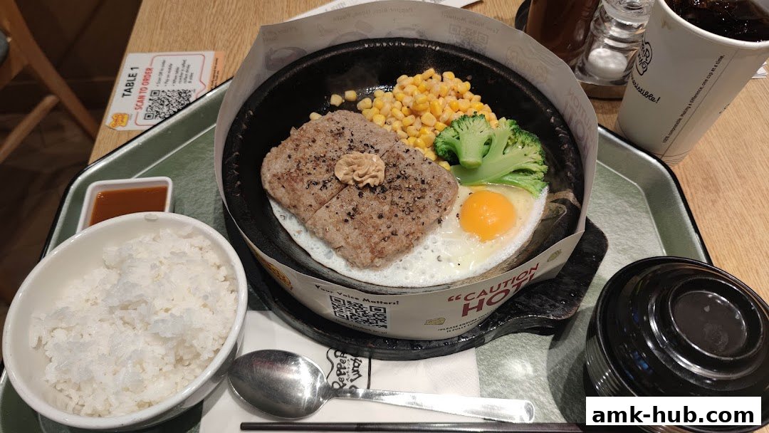 A sizzling hot plate meal with steak, egg, corn, broccoli, and rice.