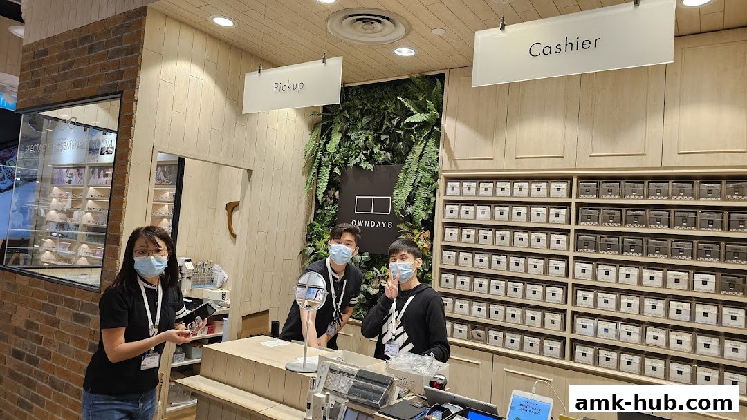 Staff at OWNDAYS AMK Hub with a wall of eyewear cases and a green wall.