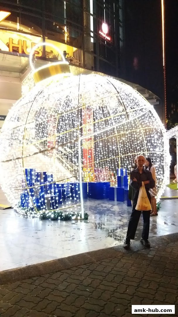 A large illuminated Christmas ornament display with people posing in front of it.