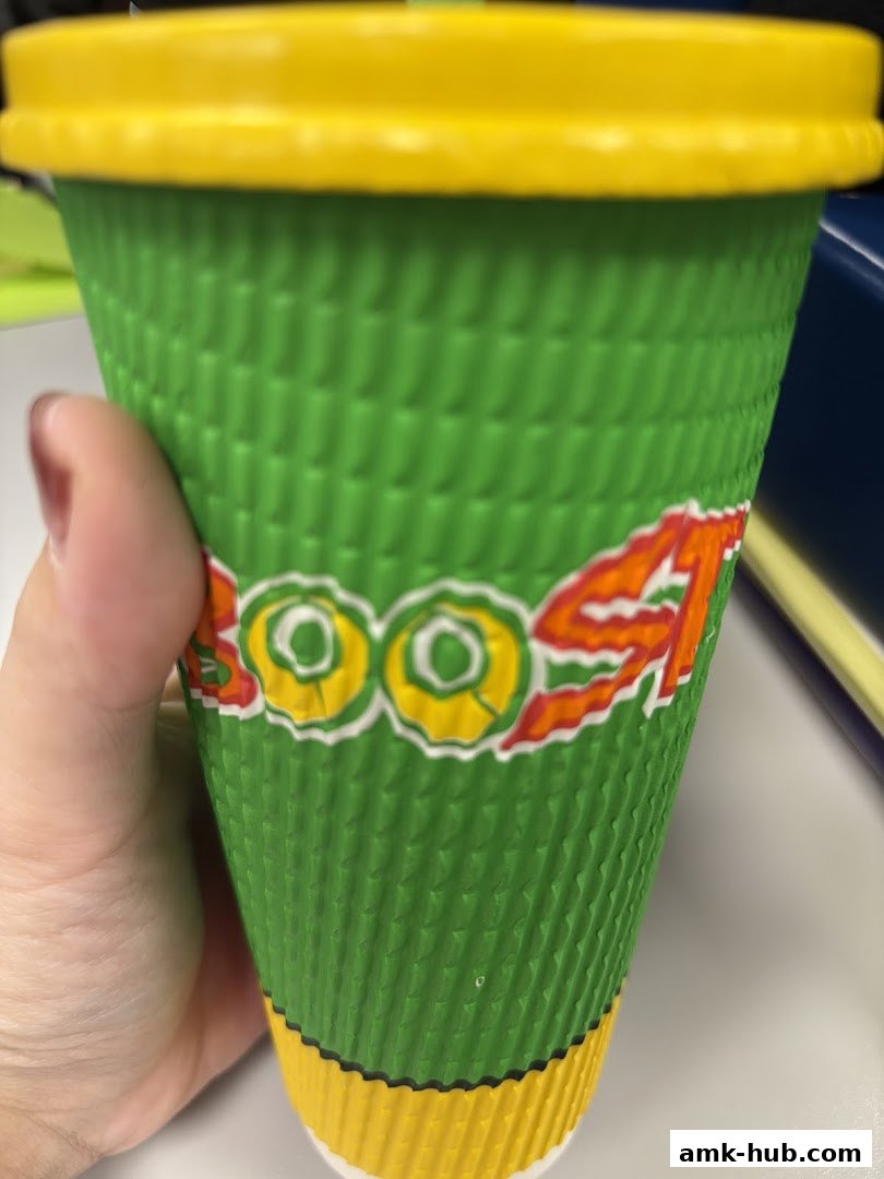 A hand holds a green and yellow Boost Juice cup with the logo visible.