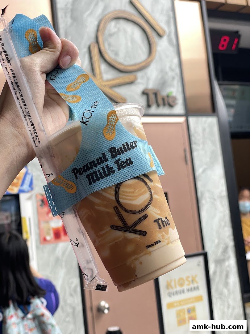 A hand holds a Peanut Butter Milk Tea from KOI Thé with the shop's logo visible.