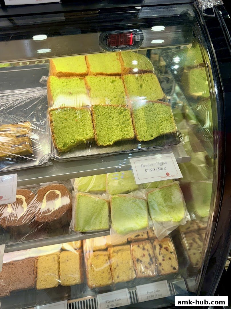 A display case filled with various slices of cake, including pandan chiffon and fruit cake.