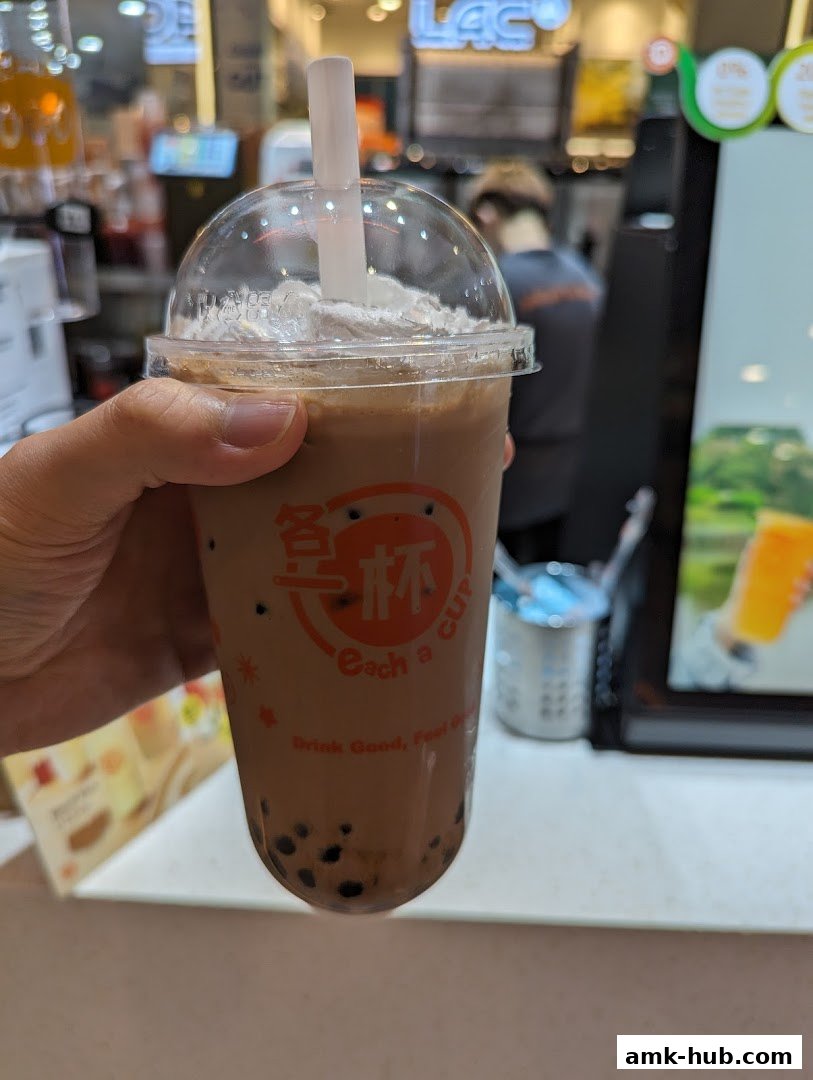 A hand holds a bubble tea drink with whipped cream and tapioca pearls.