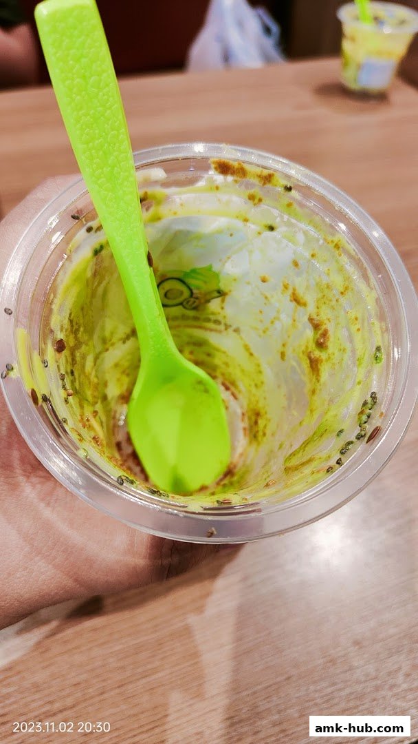 A nearly empty avocado smoothie cup with a bright green spoon and chia seeds.