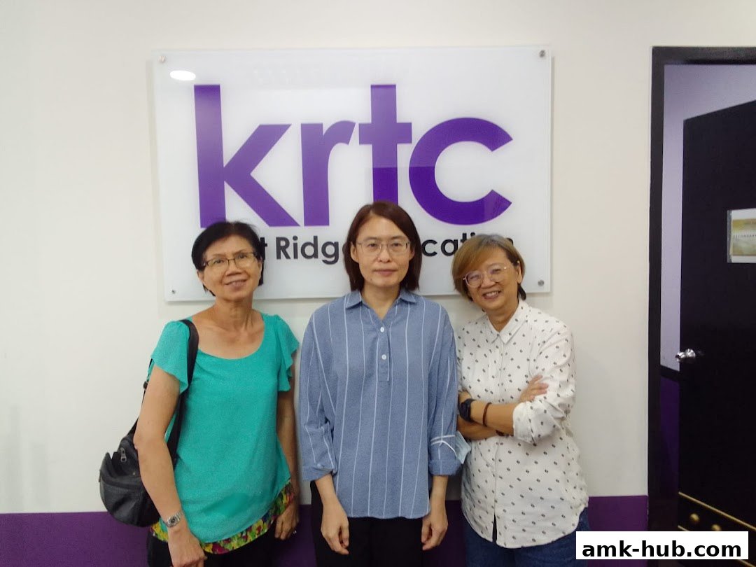Three women stand in front of a KRTC Ang Mo Kio sign.