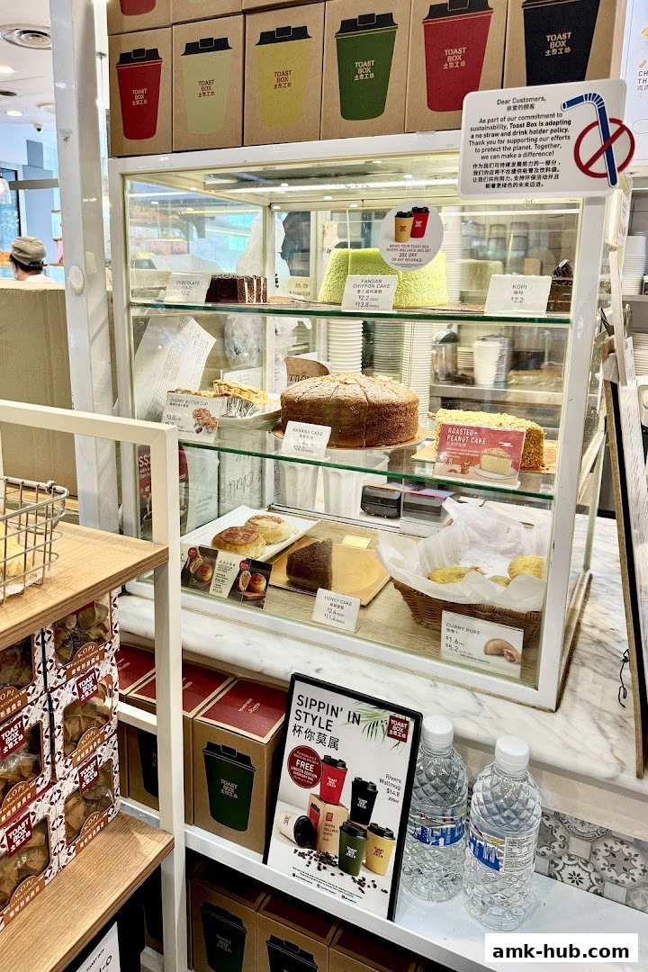 A display case filled with various cakes, pastries, and drinks at Toast Box.