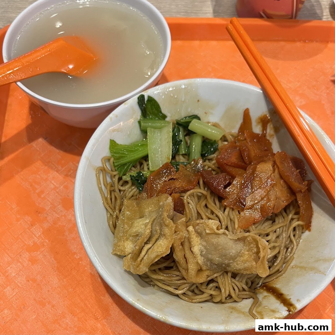 A bowl of wanton noodles with char siu, vegetables, and fried wontons, served with a side of soup.