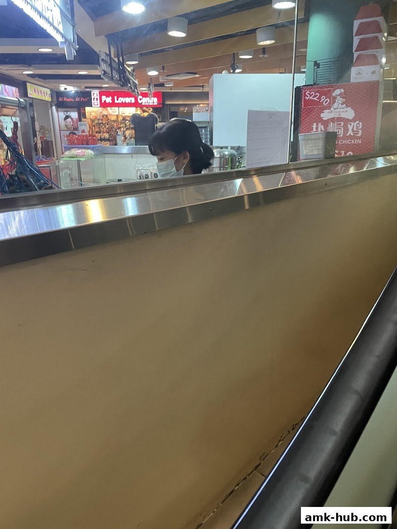 A person wearing a mask behind a counter at a food stall.