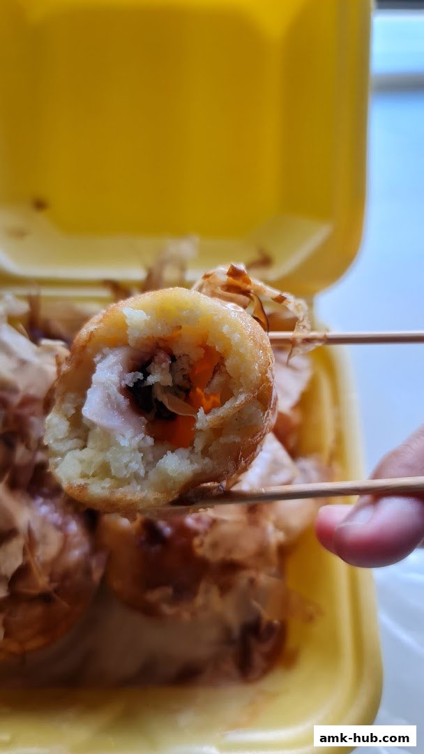 A close-up of a delicious takoyaki ball being held by chopsticks, revealing its savory filling.