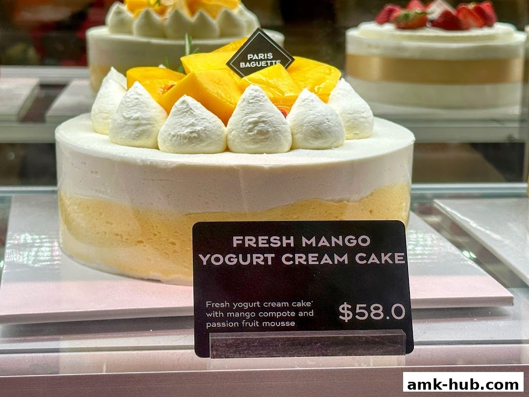A delicious Fresh Mango Yogurt Cream Cake is displayed in a bakery case.