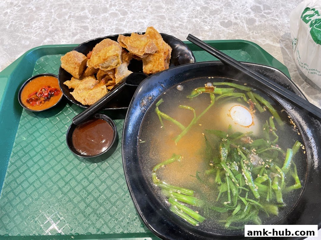 A bowl of Yong Tau Foo soup with fried wontons and dipping sauces on a tray.