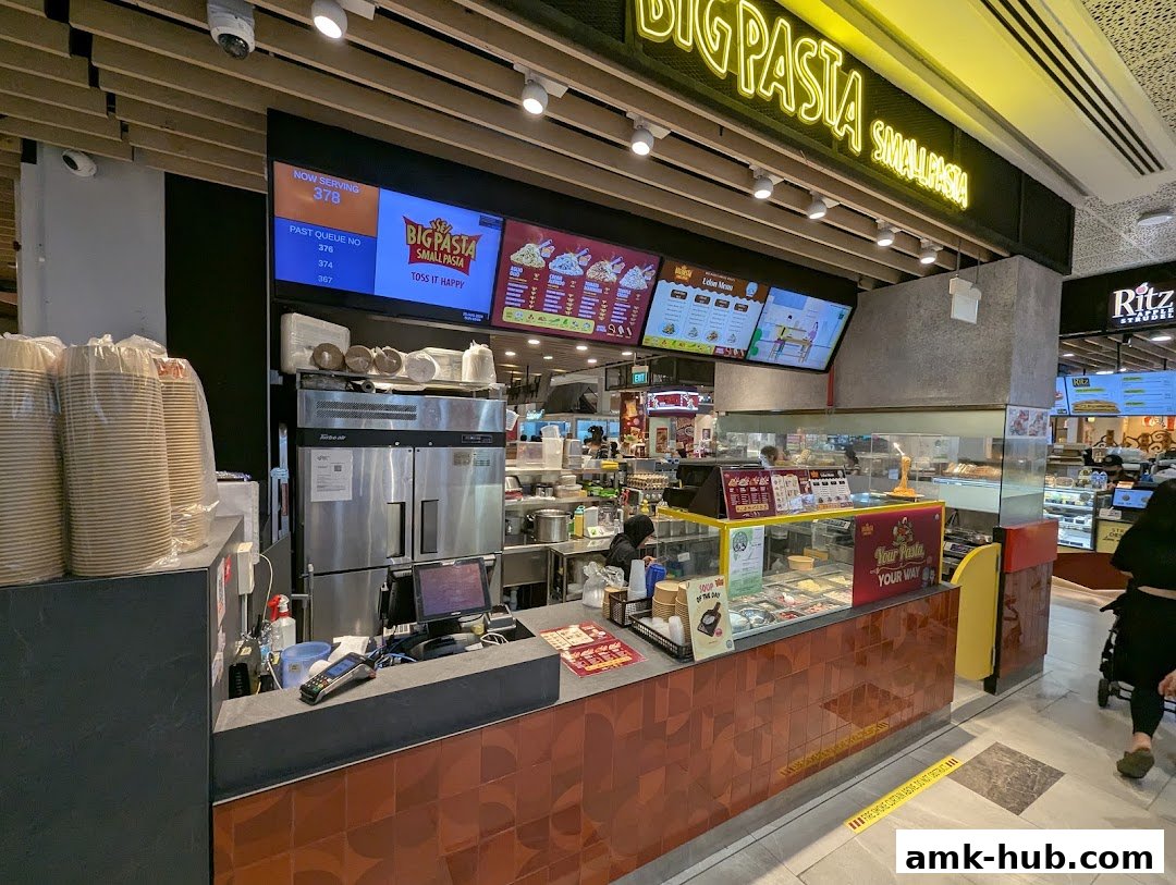 The counter and display of a pasta restaurant with digital menus and a queue display.