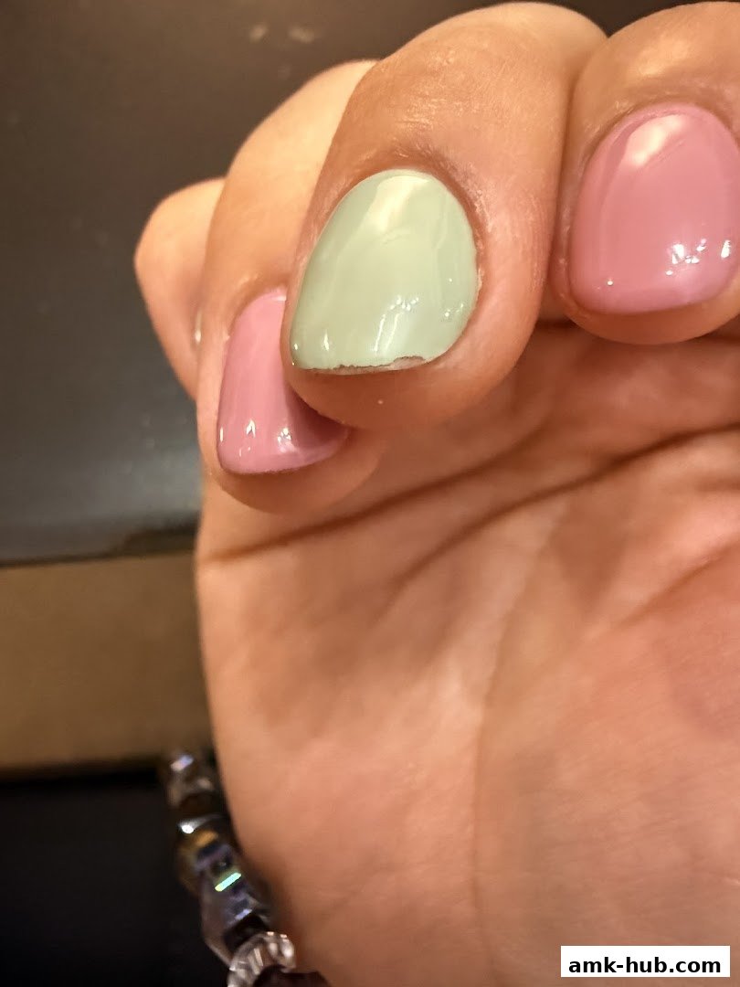 Close-up of a hand with chipped pastel green and pink nail polish.