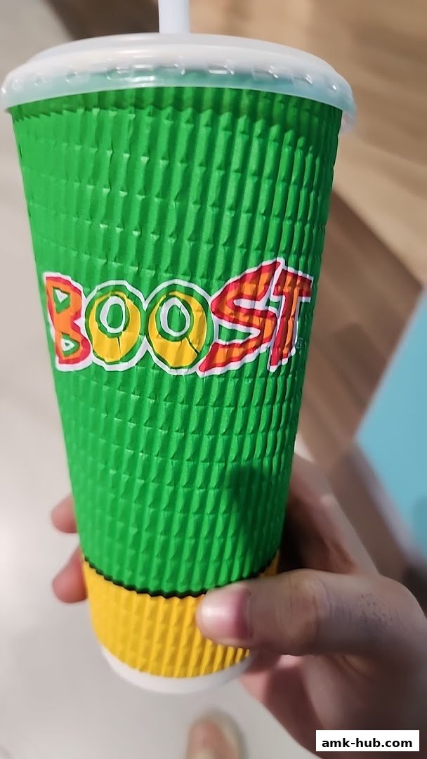 A hand holds a green and yellow cup with the Boost Juice logo.