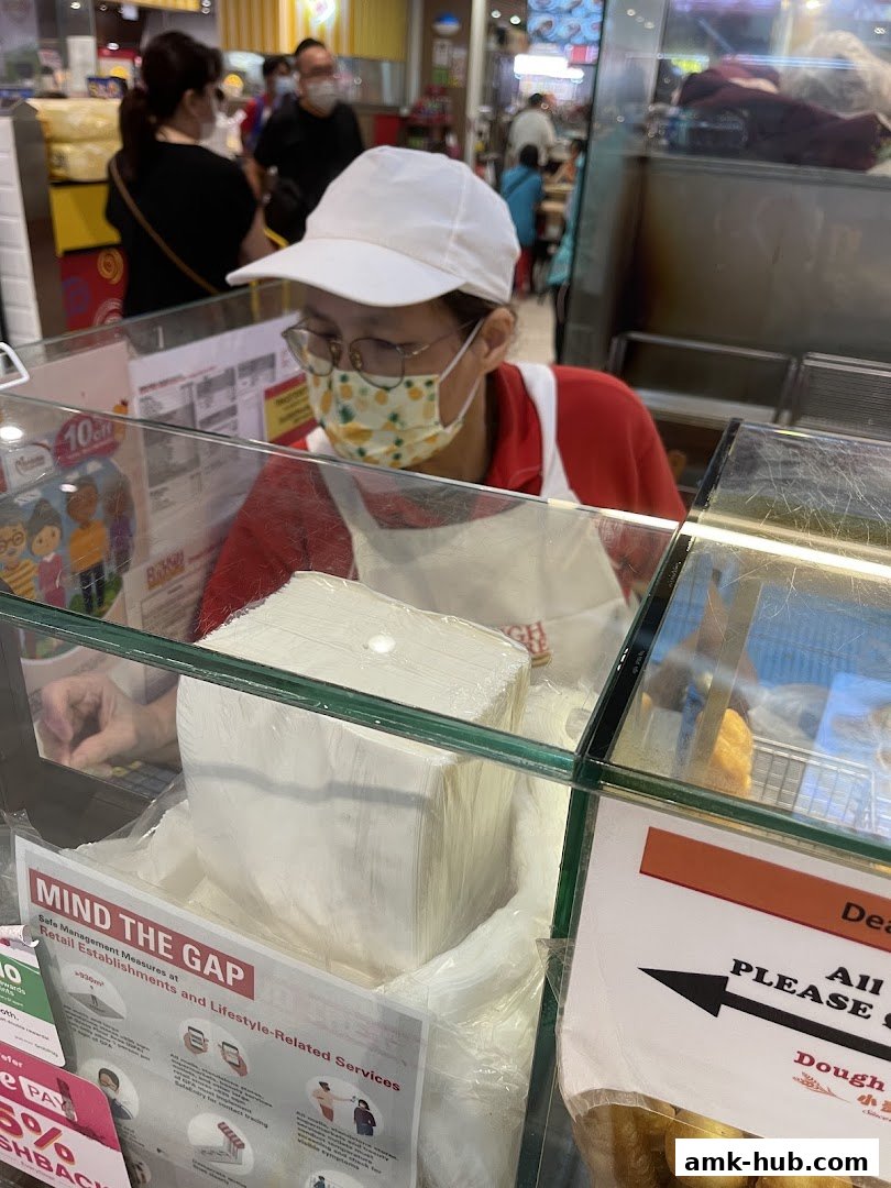 A person wearing a mask and cap works behind a glass counter at Dough Culture.
