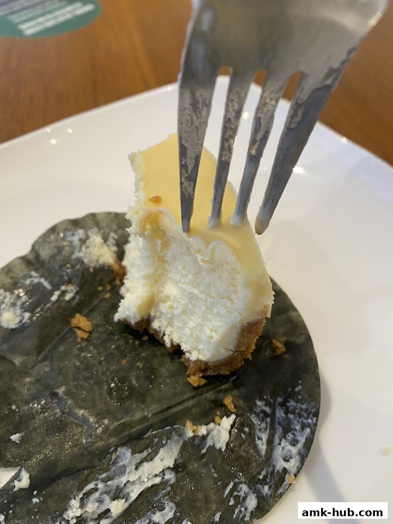 A fork is taking a bite out of a slice of cheesecake on a plate.