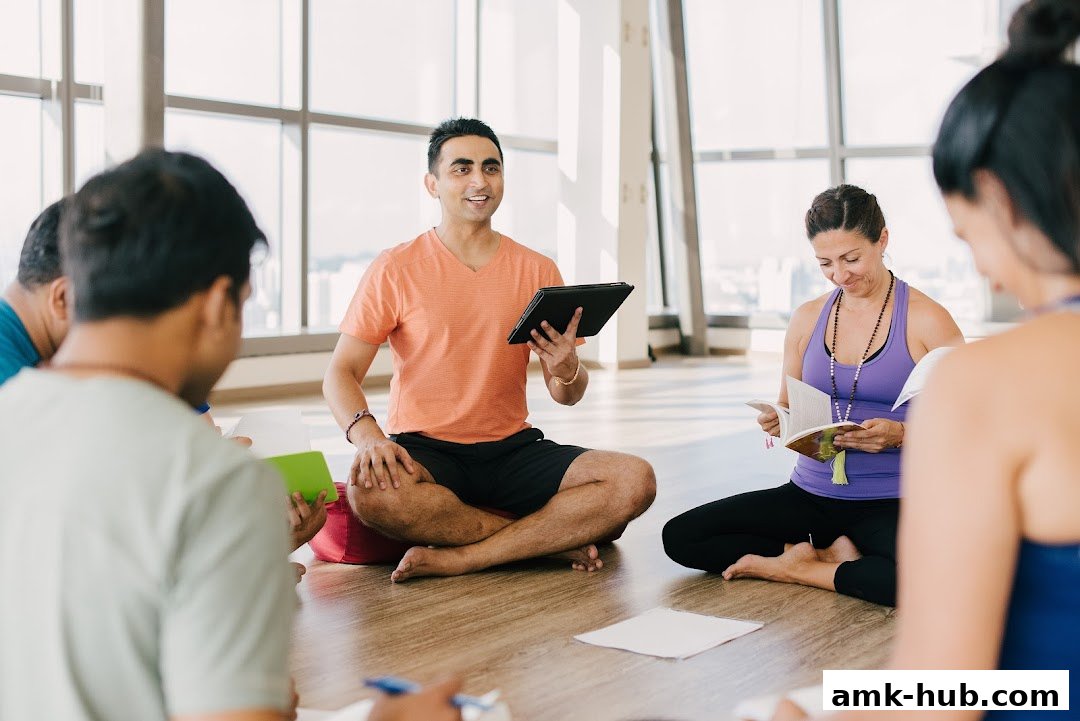 A yoga instructor leads a class, holding a tablet and speaking to students.