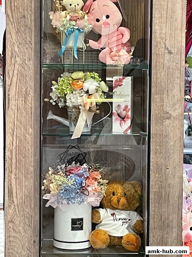 A display case featuring floral arrangements, plush toys, and chocolates, likely for gifting.