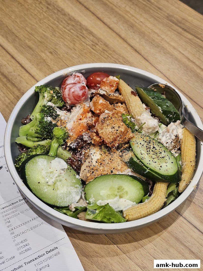 A healthy and colorful salad bowl with chicken, vegetables, and dressing on a wooden table.