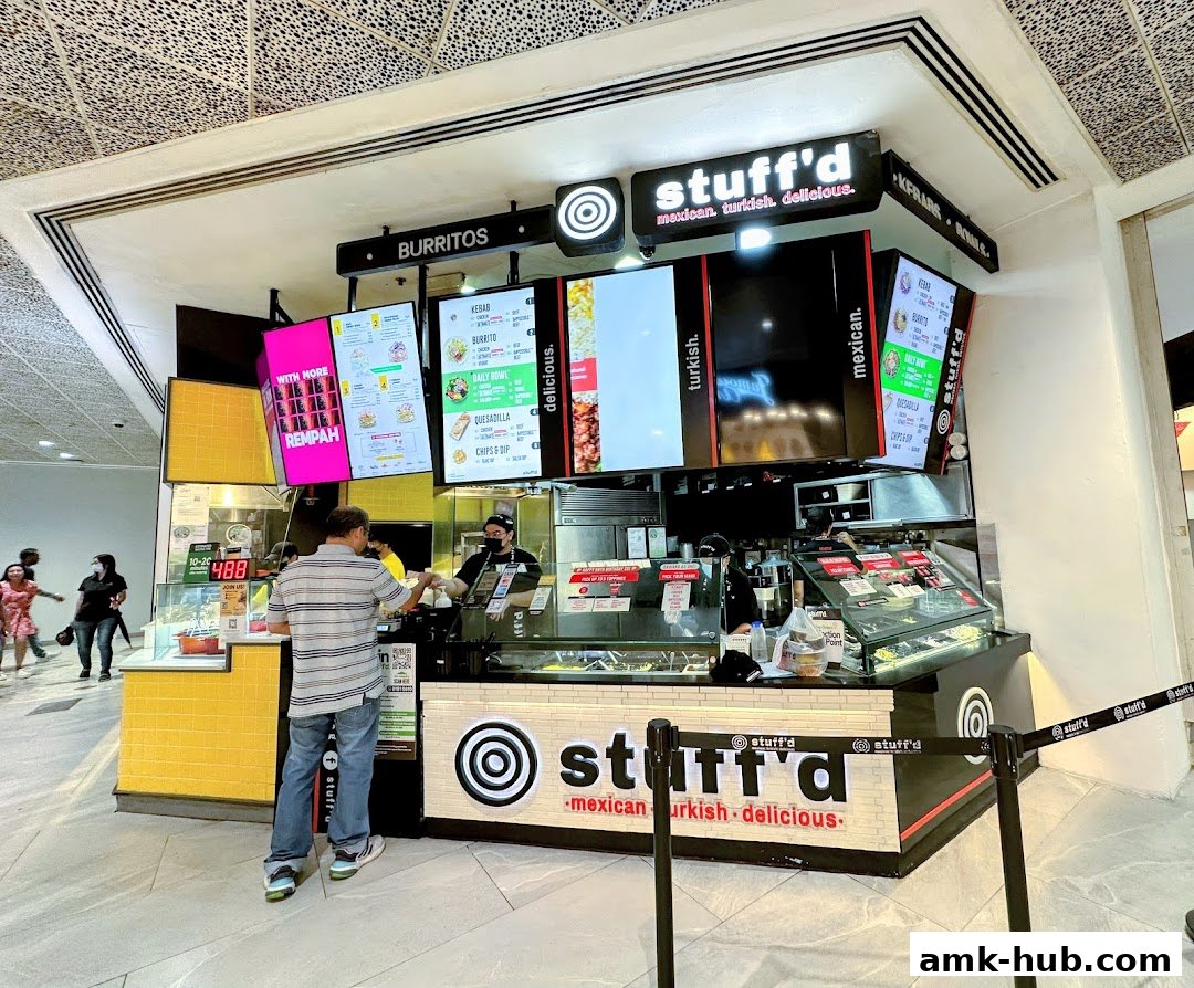 A Stuff'd More food stall with digital menus displaying food items and a customer ordering.
