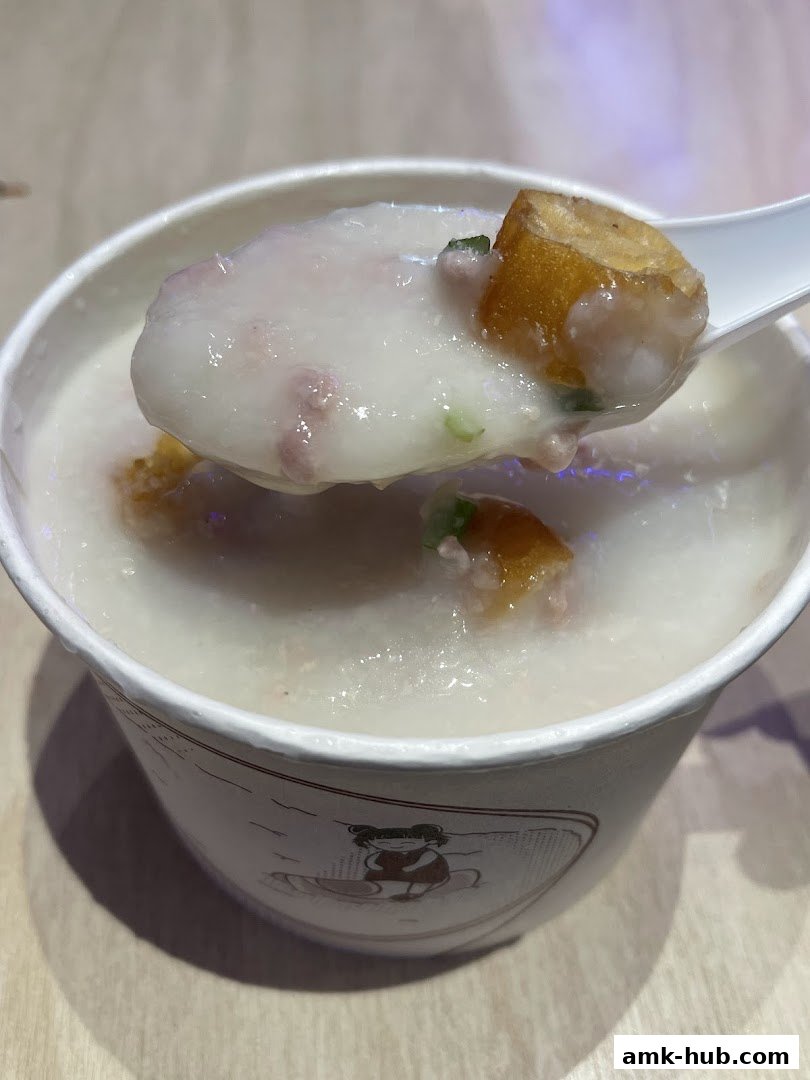 A close-up shot of a spoon lifting a portion of savory congee with fried dough sticks.
