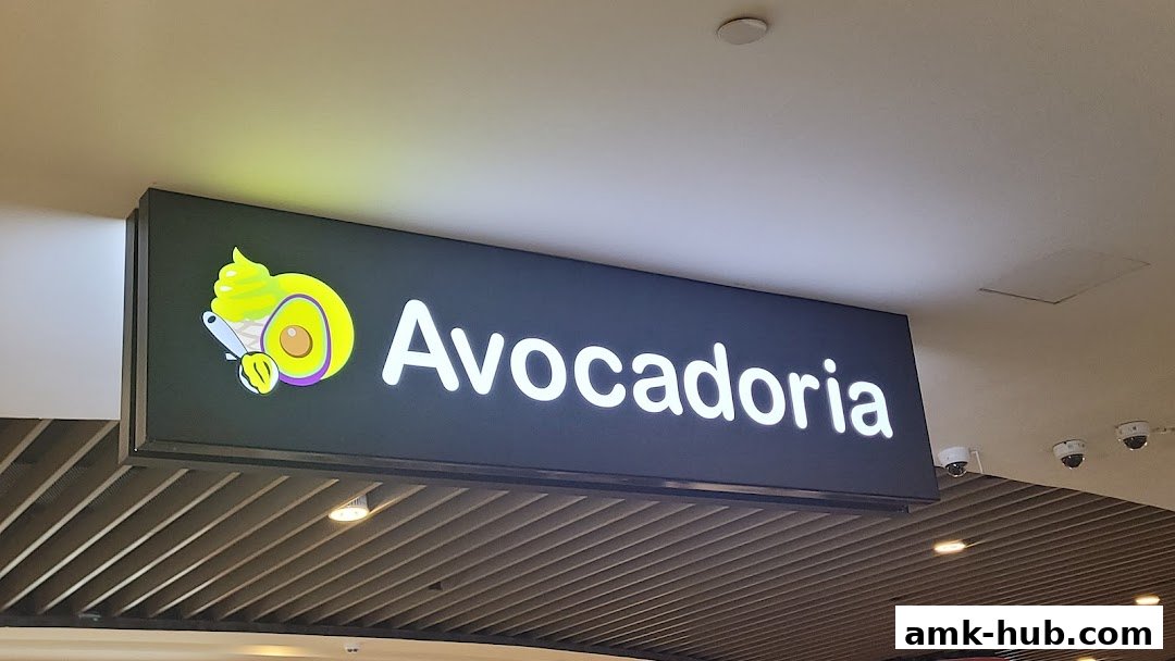 A lit sign for 'Avocadoria' featuring a stylized avocado and ice cream cone logo.