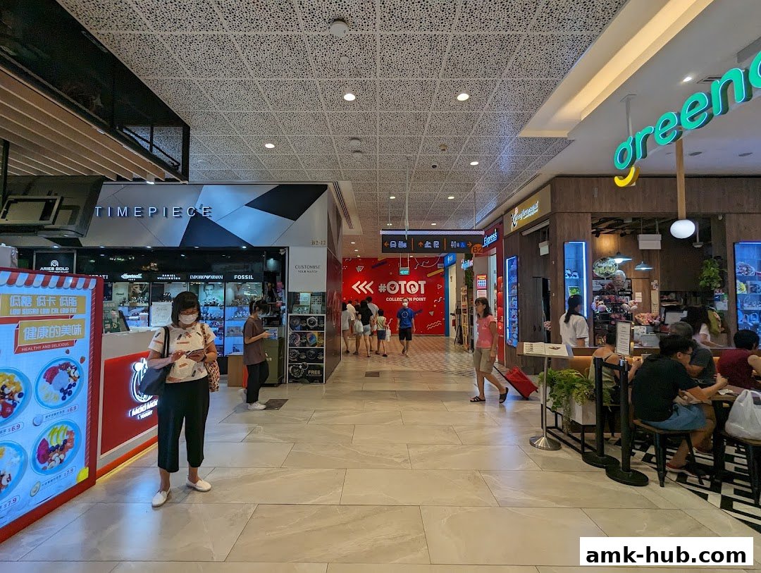A shopping mall corridor with various shops, including a timepiece store and a food outlet.