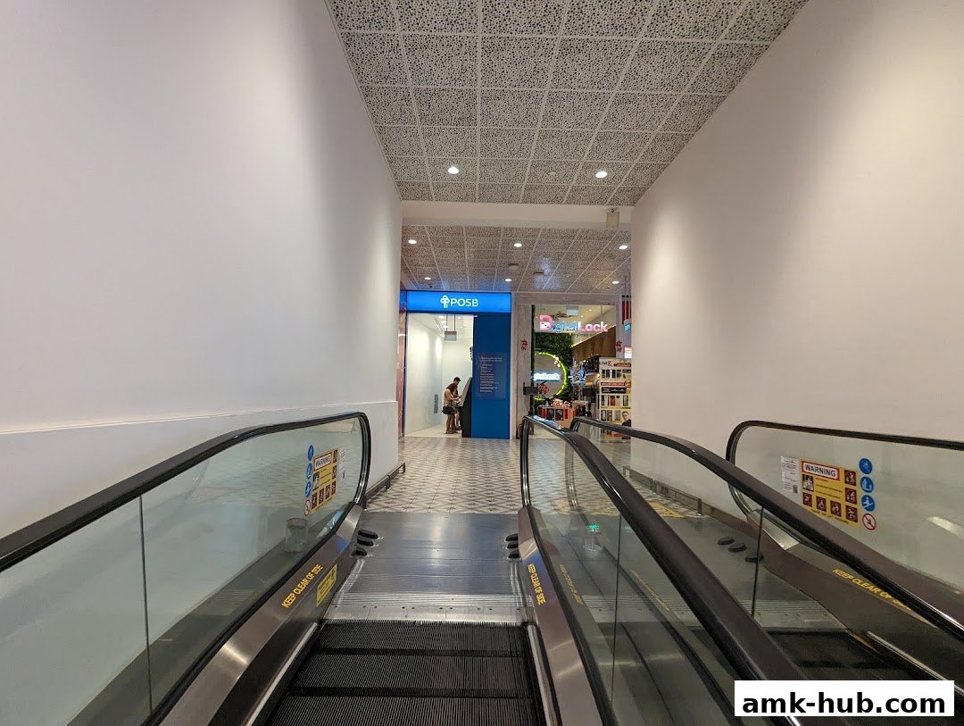 View of escalators leading towards a POSB ATM and other shops in a mall.