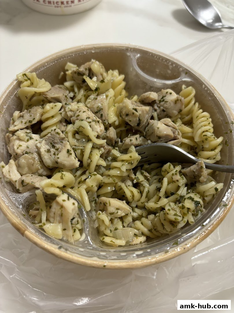 A close-up shot of a pasta dish with chicken and herbs in a to-go container.