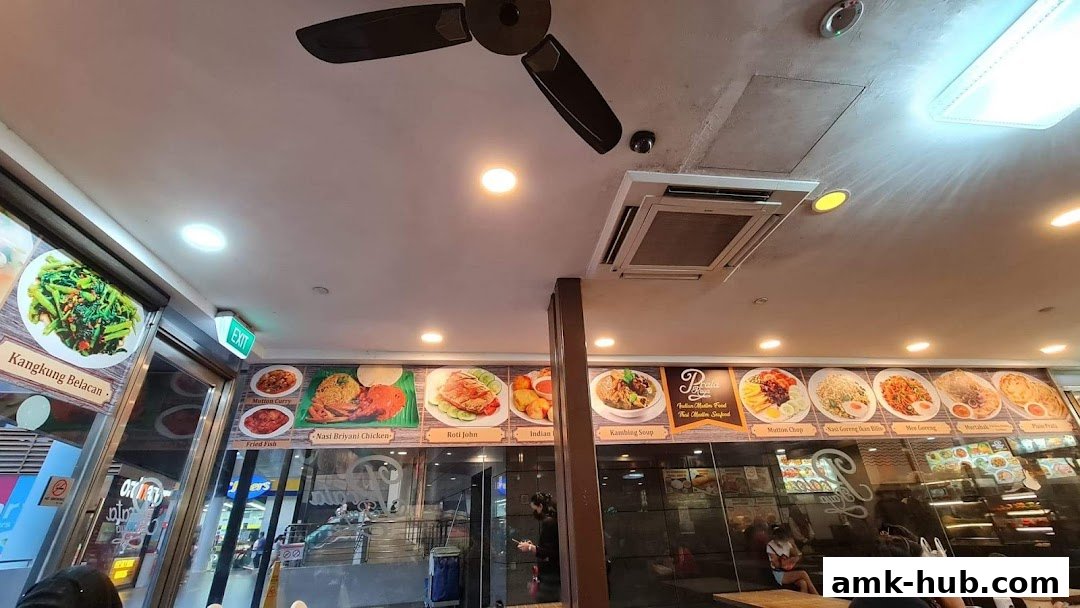 A food stall with various dishes displayed on the wall, including Kangkung Belacan and Nasi Briyani Chicken.