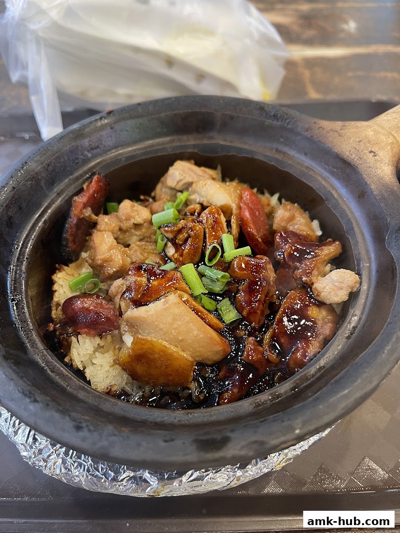 A close-up of a clay pot rice dish with chicken, sausage, and scallions.