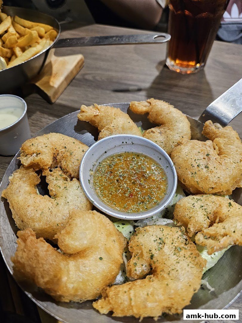 A close-up of a platter of golden-brown fried shrimp with a dipping sauce and a side of fries.