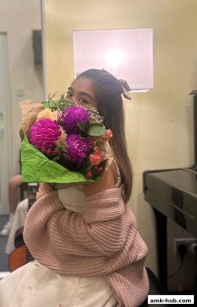 A person holds a vibrant bouquet of flowers in front of their face, with a piano in the background.